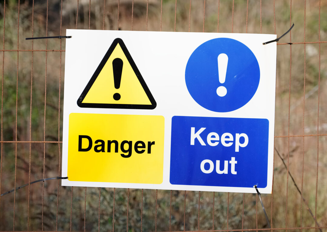 Danger keep out safety sign on fence at construction building site.
