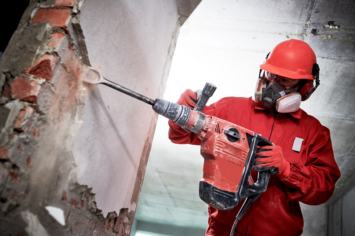 Demolition and destroying. Worker with demolition hammer in personal protection equipment removing interior brick wall plastering.
